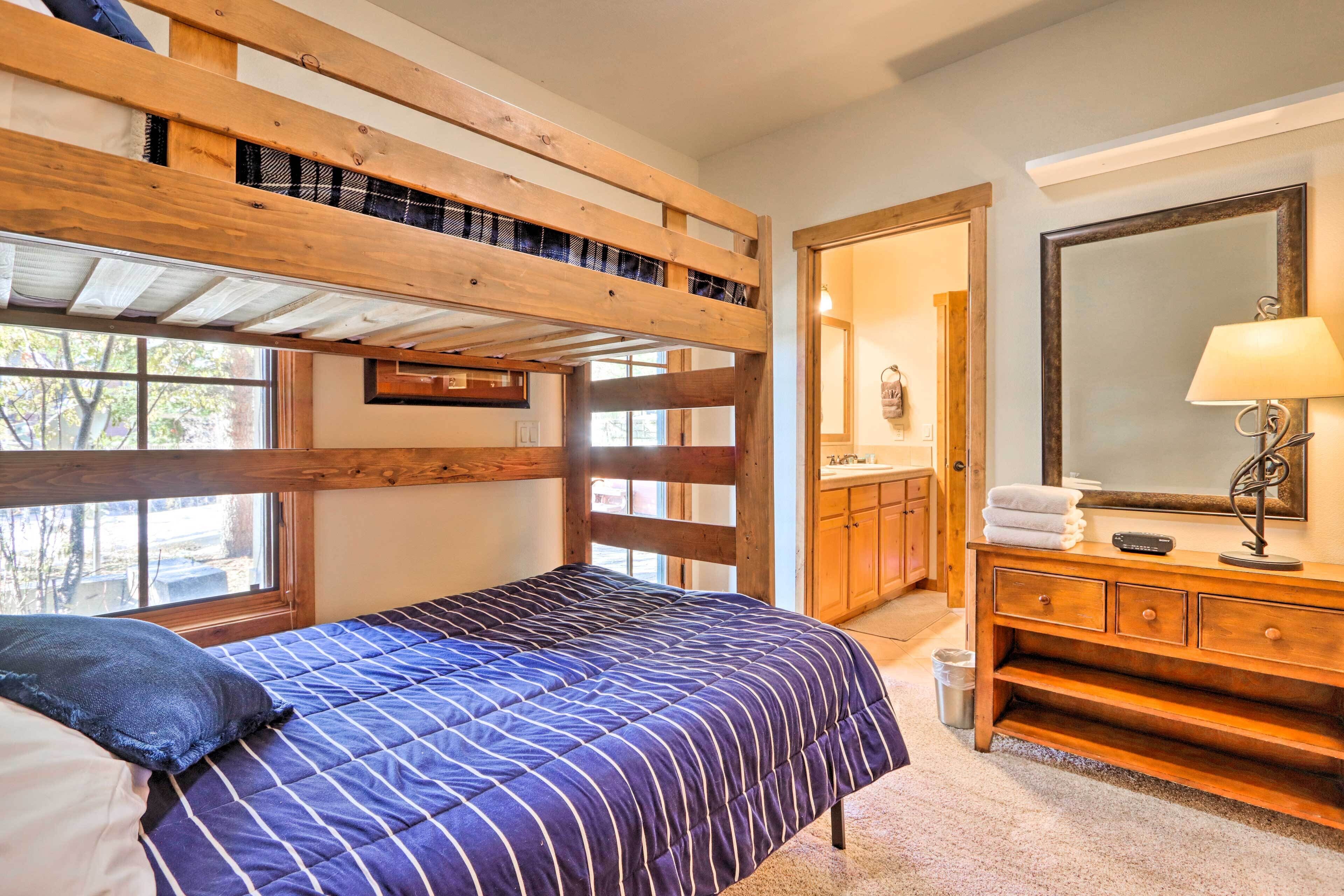 Ein Stockbett mit blauen Streifen, eine Holzkommode mit Spiegel und ein Fenster mit Blick auf Bäume.