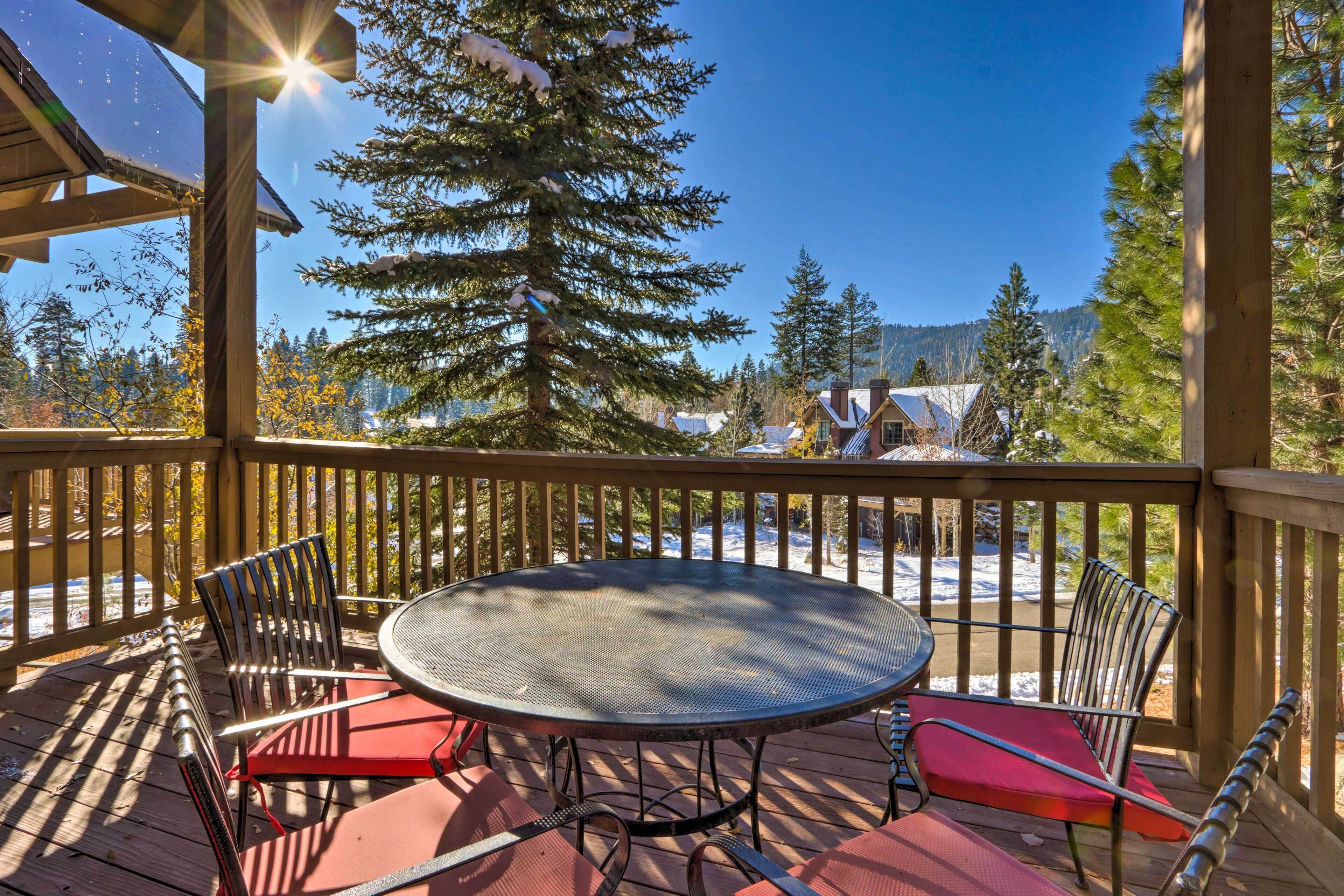 A wooden deck with a round table and chairs, overlooking a snowy landscape and trees.