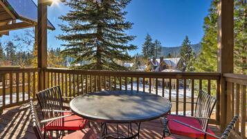A wooden deck with a round table and chairs, overlooking a snowy landscape and trees.