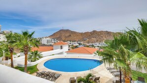 A pool area with lounge chairs, palm trees, and a mountain view. - Chic Cabo Condo - Walk to Marina & Downtown! (Cabo San Lucas)
