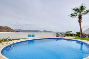 A swimming pool with a view of mountains, a palm tree, and lounge chairs. - Chic Cabo Condo - Walk to Marina & Downtown! (Cabo San Lucas)