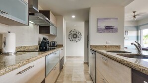 A modern kitchen with granite countertops, stainless steel appliances, and a decorative wall piece. - Chic Cabo Condo - Walk to Marina & Downtown! (Cabo San Lucas)