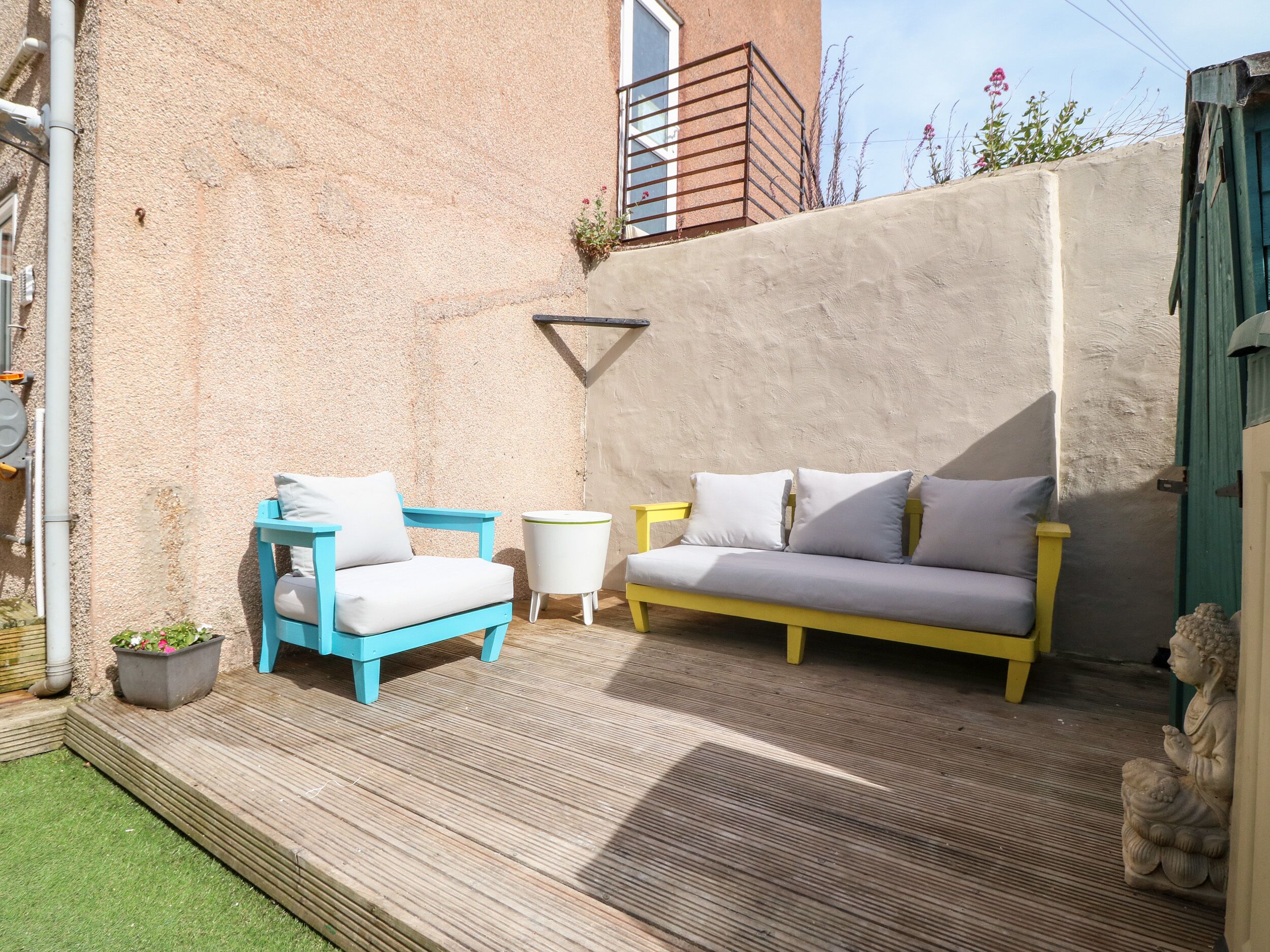 A patio with a blue and yellow sofa, a white armchair, and a small round table.