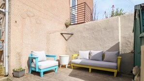 A patio with a blue and yellow sofa, a white armchair, and a small round table.