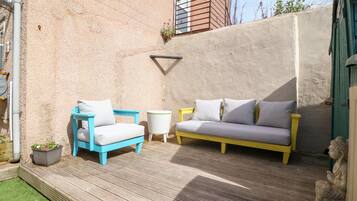 A patio with a blue and yellow sofa, a white armchair, and a small round table.
