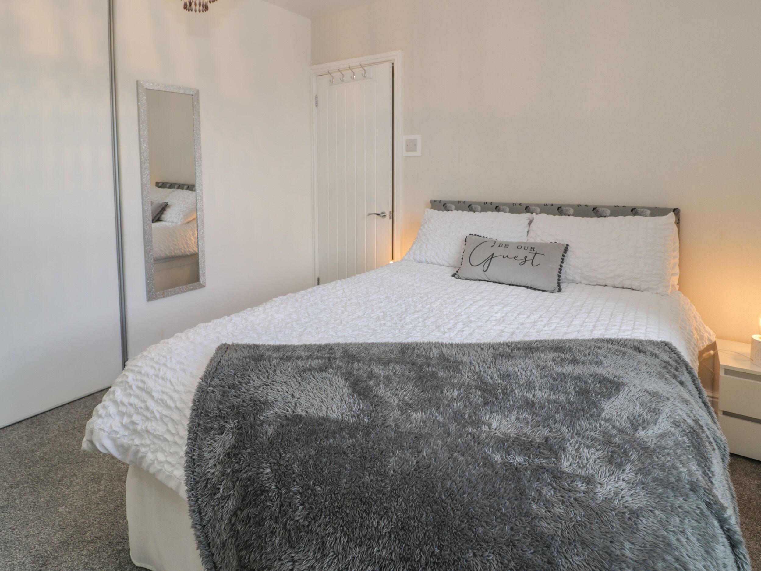 Un dormitorio con cama, espejo, puerta y mesita de noche.
