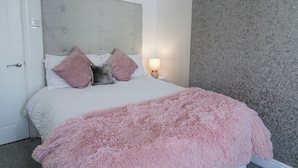 A bedroom with a bed, a headboard, a nightstand, a lamp, and a patterned wall.
