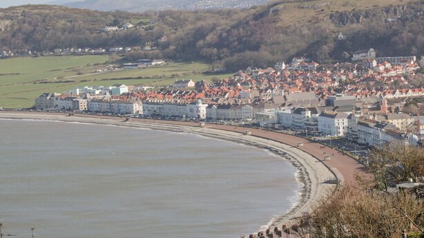 A coastal town with a prominent waterfront, historic buildings, and rolling hills in the background.