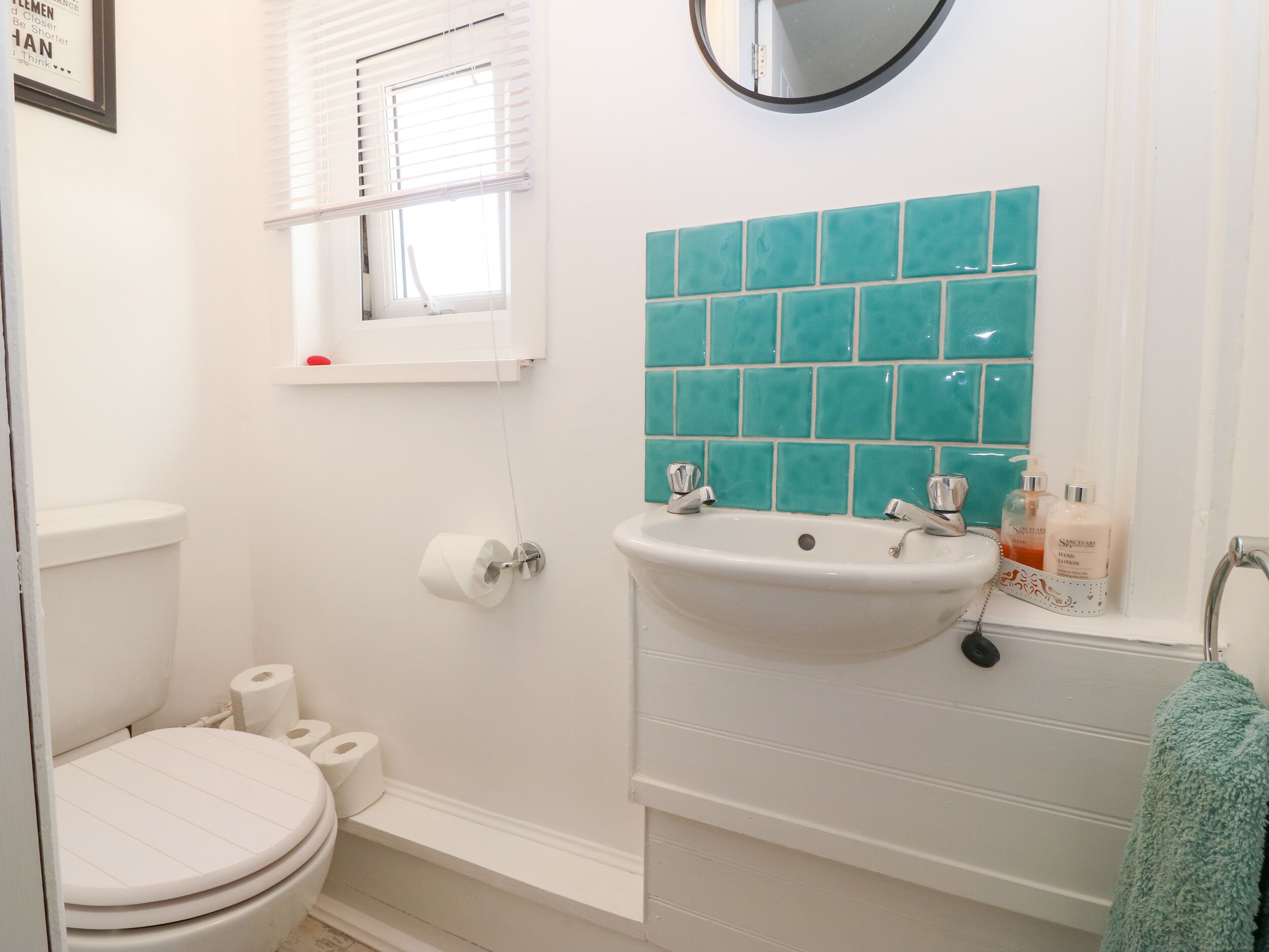 A bathroom with a toilet, sink, and a window with blinds.
