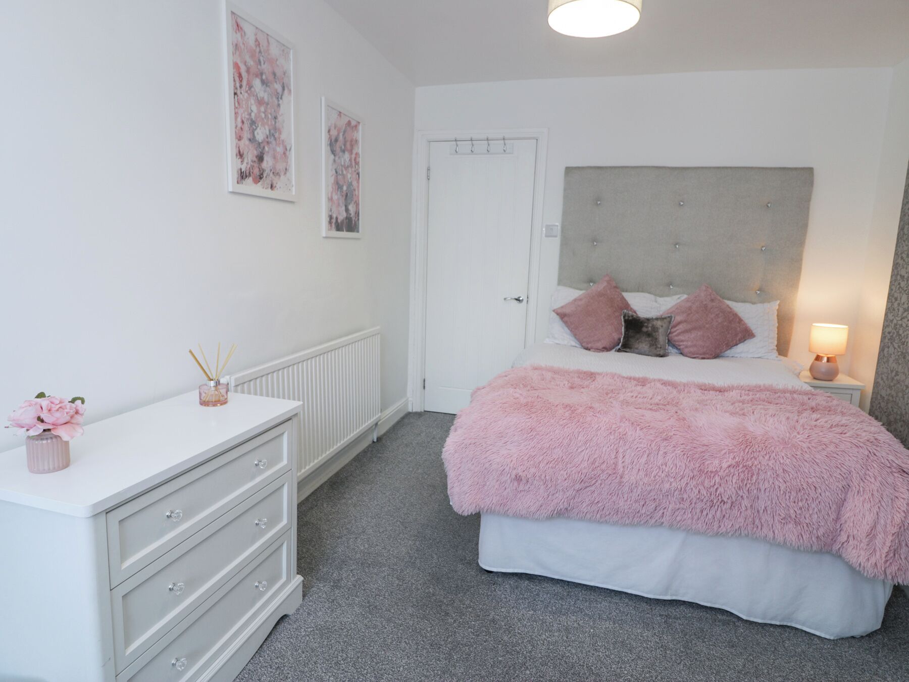 A bedroom with a bed, a dresser, a nightstand, and a door.