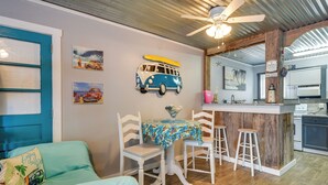A room with a bed, a dining table with chairs, a kitchen area, and artwork on the walls. - 1 Mi to Ocean Isle Beach! Studio w/ Outdoor Oasis (Ocean Isle Beach)