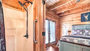 A wooden cabin interior with a bathroom featuring a shower and a bedroom with a bed and a wall-mounted deer head decoration. - 'star Lite' Cabin: Hot Tub, Deck & Pool Table (Sevierville)