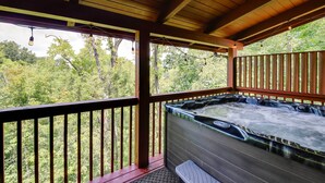 A hot tub under a wooden deck with a view of a forest. - 'star Lite' Cabin: Hot Tub, Deck & Pool Table (Sevierville)