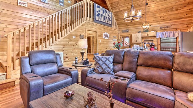 A log cabin interior with a wooden staircase, leather sofas, a dining area, and a kitchen. - 'star Lite' Cabin: Hot Tub, Deck & Pool Table (Sevierville)