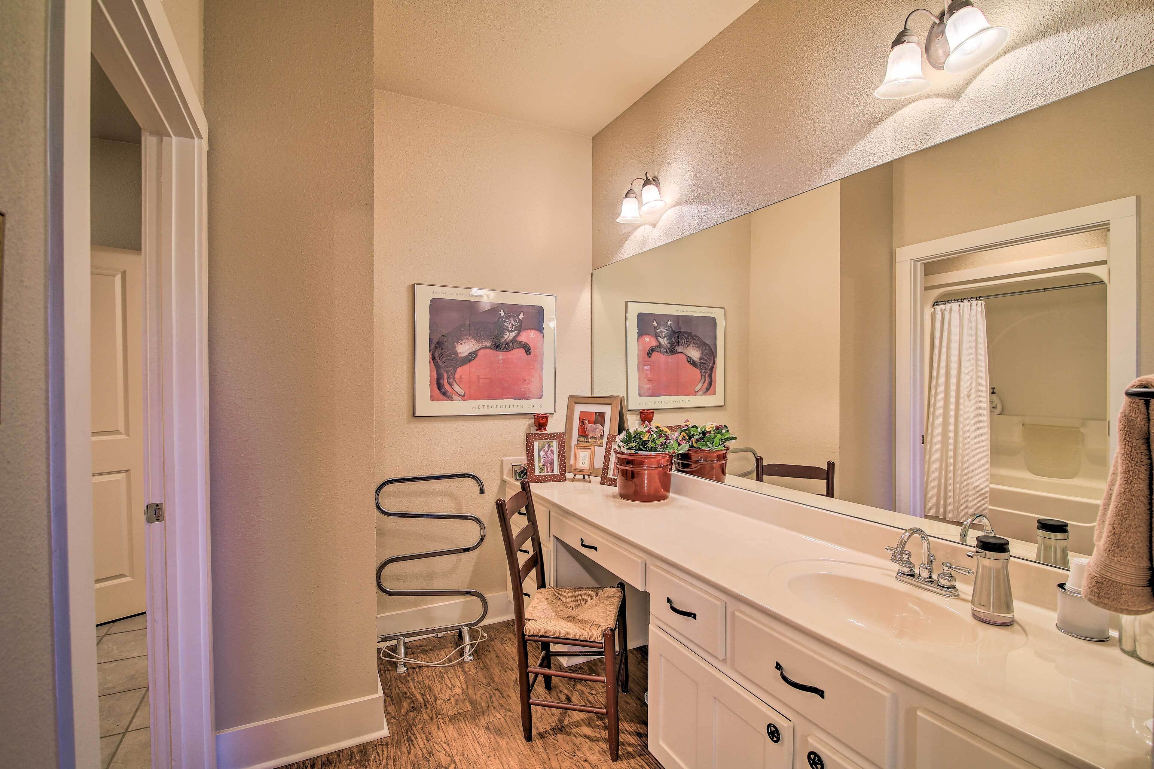 A bathroom with a large mirror, a sink, and a chair. There are framed pictures on the wall and a towel rack.