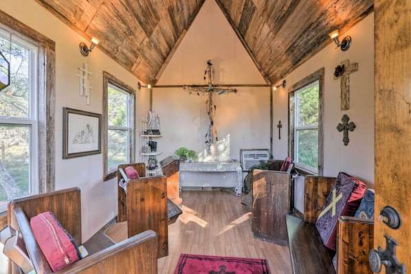 A rustic interior with wooden pews, a wooden altar, and a cross on the wall.