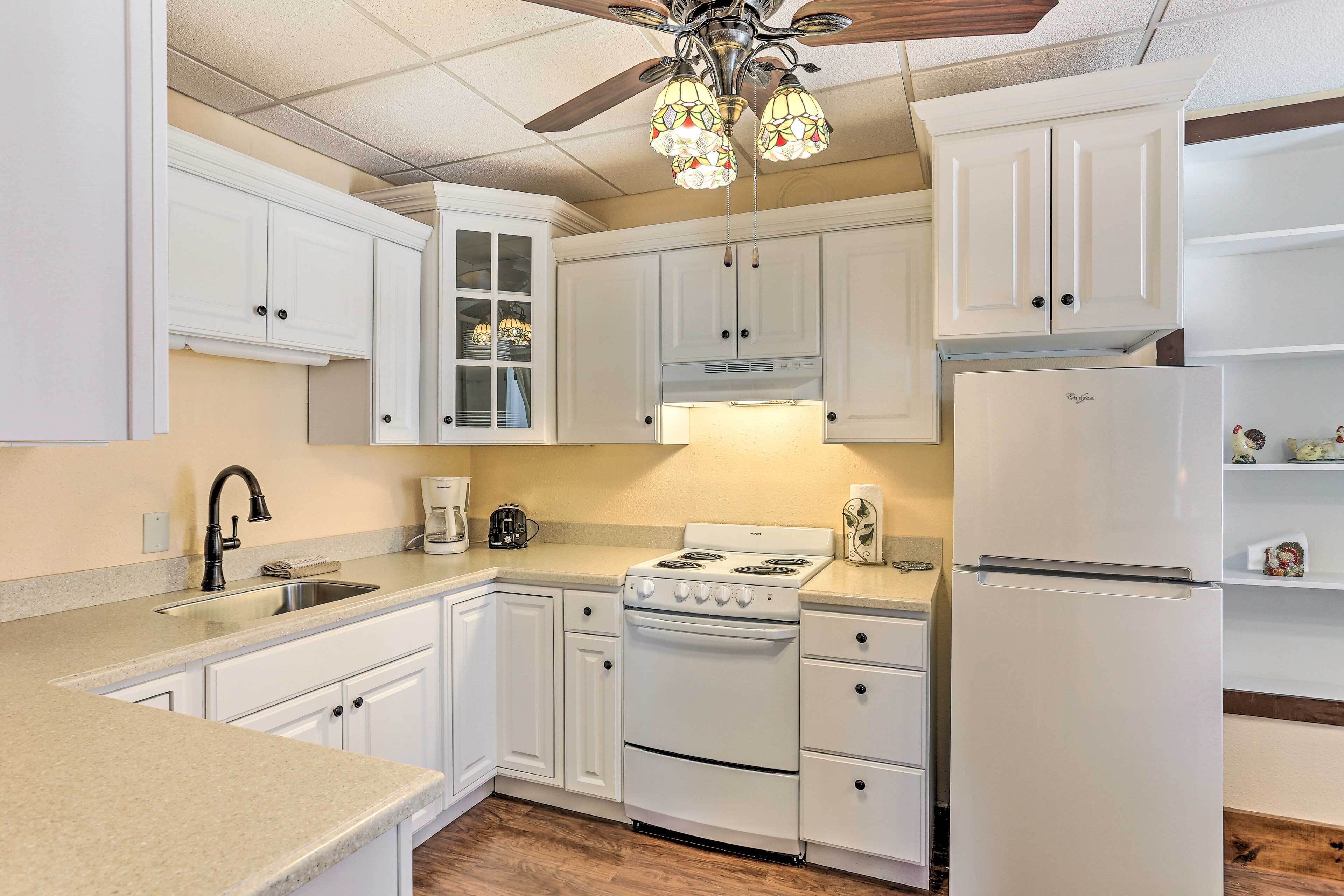 A kitchen with white cabinets, a stove, a refrigerator, and a ceiling fan.