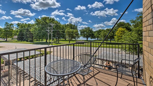 Ein Balkon mit einem Metalltisch und -stühlen, mit Blick auf einen Park mit Bäumen und einem See.