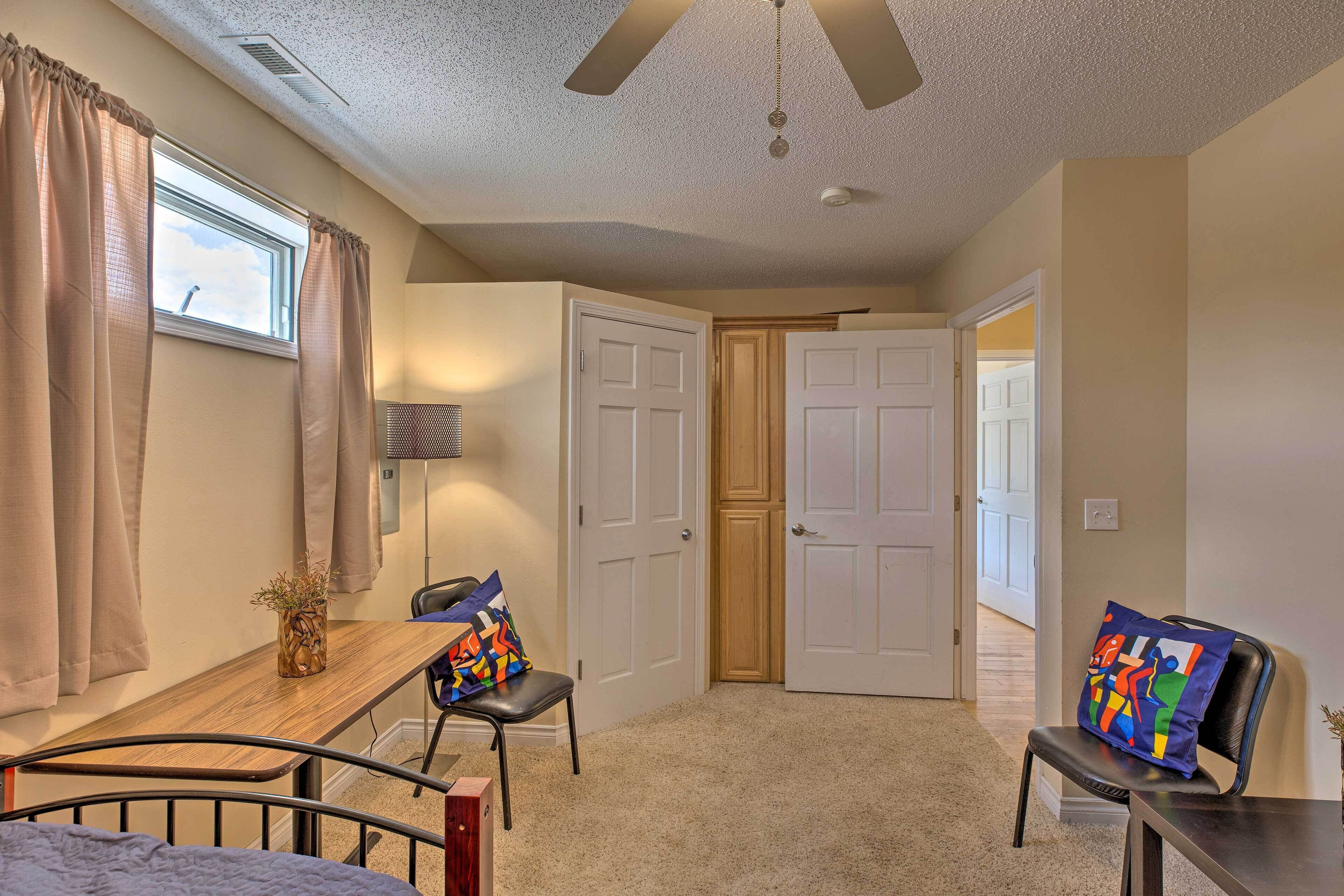 A bedroom with a bed, a desk, a chair, a ceiling fan, and a window with curtains.