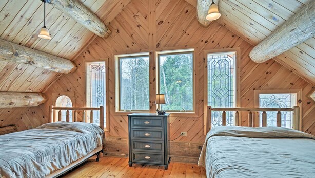 Une chambre dans une cabane en bois, avec deux lits, une commode et de grandes fenêtres.