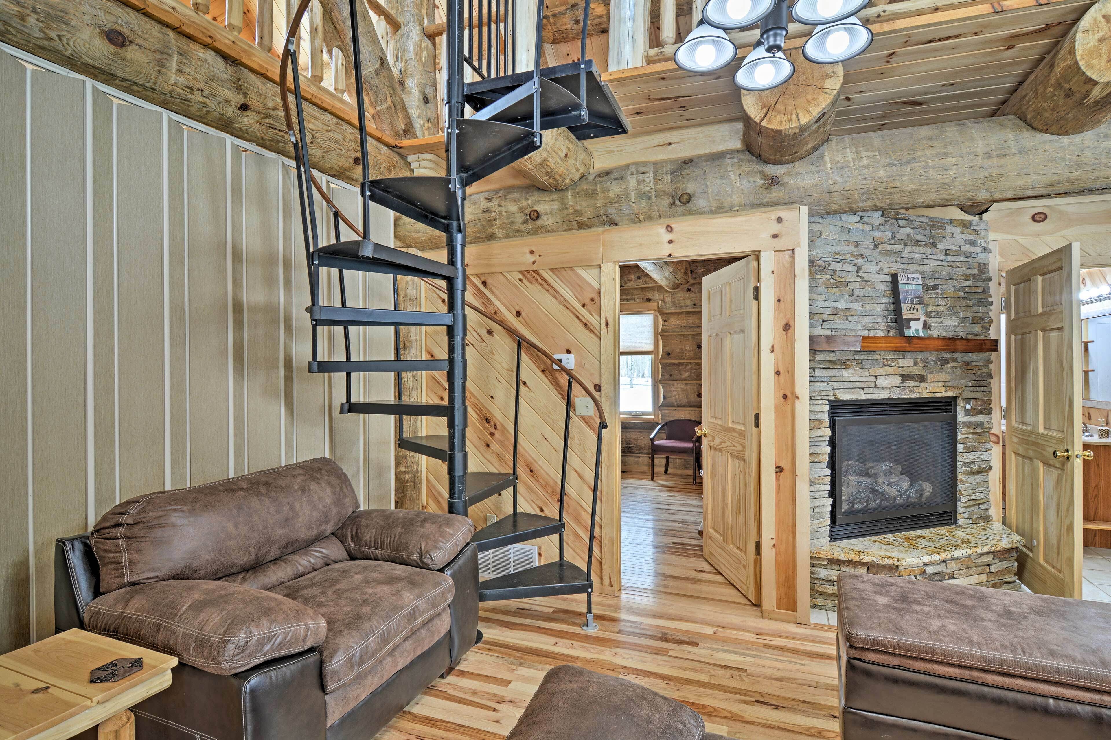 A cozy cabin interior with a stone fireplace, a leather sofa, and a spiral staircase.