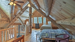 Ein gemütliches Schlafzimmer im Dachgeschoss mit Holzbalken, zwei Betten, einem Schreibtisch und einem Stuhl.