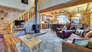 A spacious living area with a wooden staircase, a fireplace, a kitchen, and a dining area. - Peaceful Garden Valley Cabin w/ Private Deck! (Garden Valley)