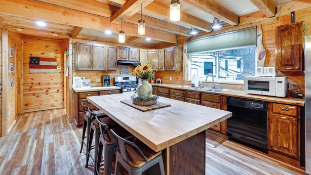 A wooden cabin kitchen with a central island, bar stools, a microwave, and a dishwasher. - Peaceful Garden Valley Cabin w/ Private Deck! (Garden Valley)