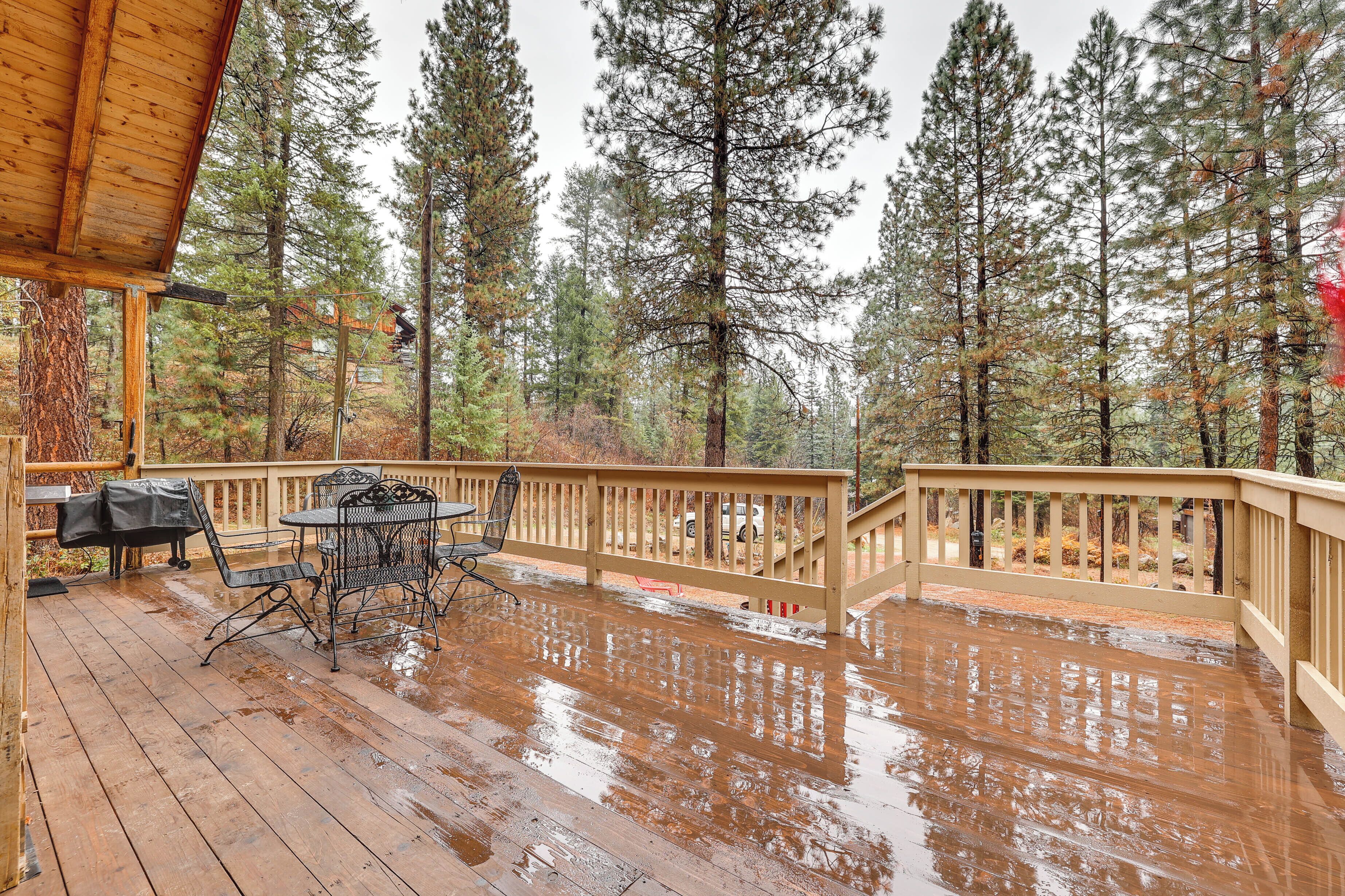 A wooden deck with a table and chairs, surrounded by tall trees.