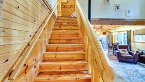 A wooden staircase with a handrail leading to a living area with a fireplace, a sofa, and a dining table. - Peaceful Garden Valley Cabin w/ Private Deck! (Garden Valley)