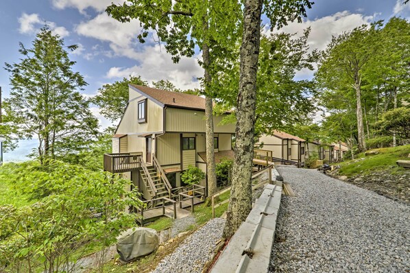 A row of cabins with wooden decks and stairs, surrounded by trees and a gravel path.