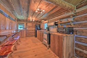 Interior rústico de uma cabana de madeira, com cozinha, bancos de madeira e ventilador de teto.