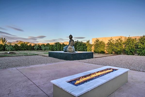 A fire feature in a rectangular stone planter, a statue on a pedestal, and a landscaped garden with trees and shrubs.