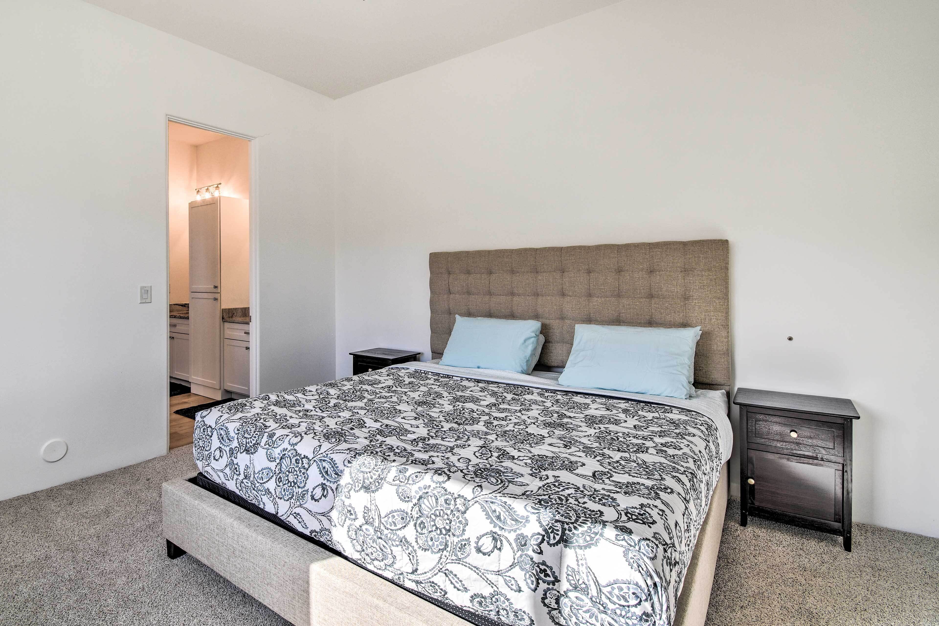 A bedroom with a bed, two nightstands, a headboard, and a door leading to a bathroom.