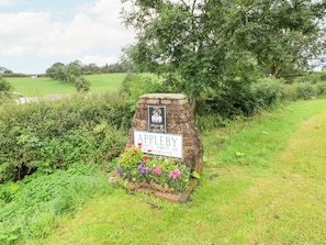Um sinal de pedra com a inscrição 'Appleby' e 'Cidade do Condado de Westmorland', rodeado por vegetação e flores.