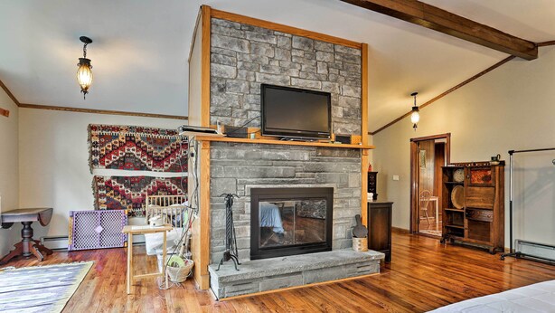 A room with a stone fireplace, wooden beams, a television on the mantel, and a bed with a white comforter. - Wawayanda House on 62 Acres - Multiple Fireplaces! (Middletown)