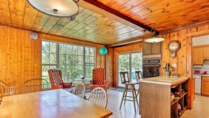 A wooden cabin interior with a dining area, kitchen, and large windows. - Wawayanda House on 62 Acres - Multiple Fireplaces! (Middletown)