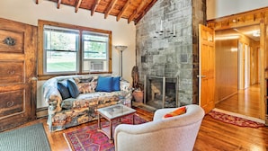 A cozy living room with a stone fireplace, wooden beams, and a large window. - Wawayanda House on 62 Acres - Multiple Fireplaces! (Middletown)