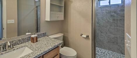 Un bagno con un piano di lavoro in granito, un WC bianco, una cabina doccia in vetro e uno specchio con illuminazione.