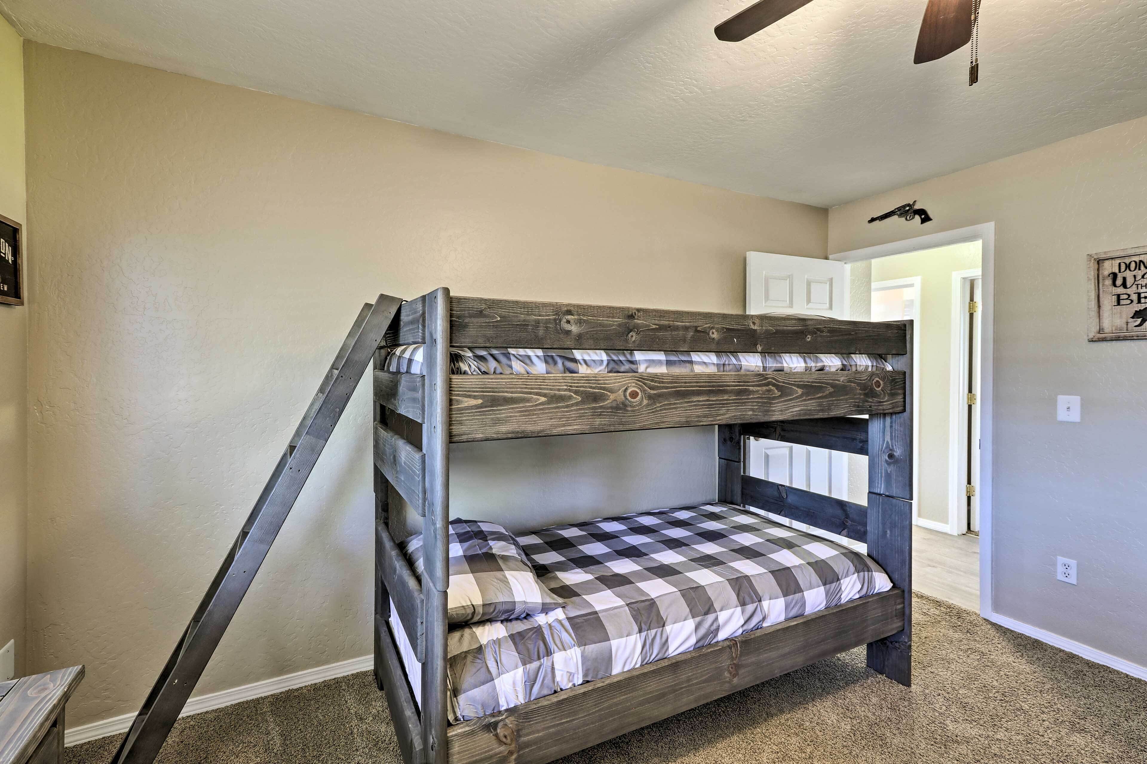 A bunk bed with a ladder, checkered bedding, and a ceiling fan in a room with beige walls and carpet.
