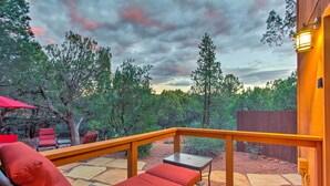 A deck with a wooden railing, a red cushioned lounge chair, and a small table.