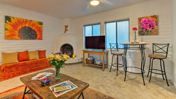 A living room with a fireplace, a television, a coffee table with magazines, and a sofa with orange cushions.