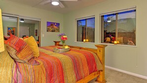 A bedroom with a bed, a ceiling fan, a window with a view, and a painting on the wall.