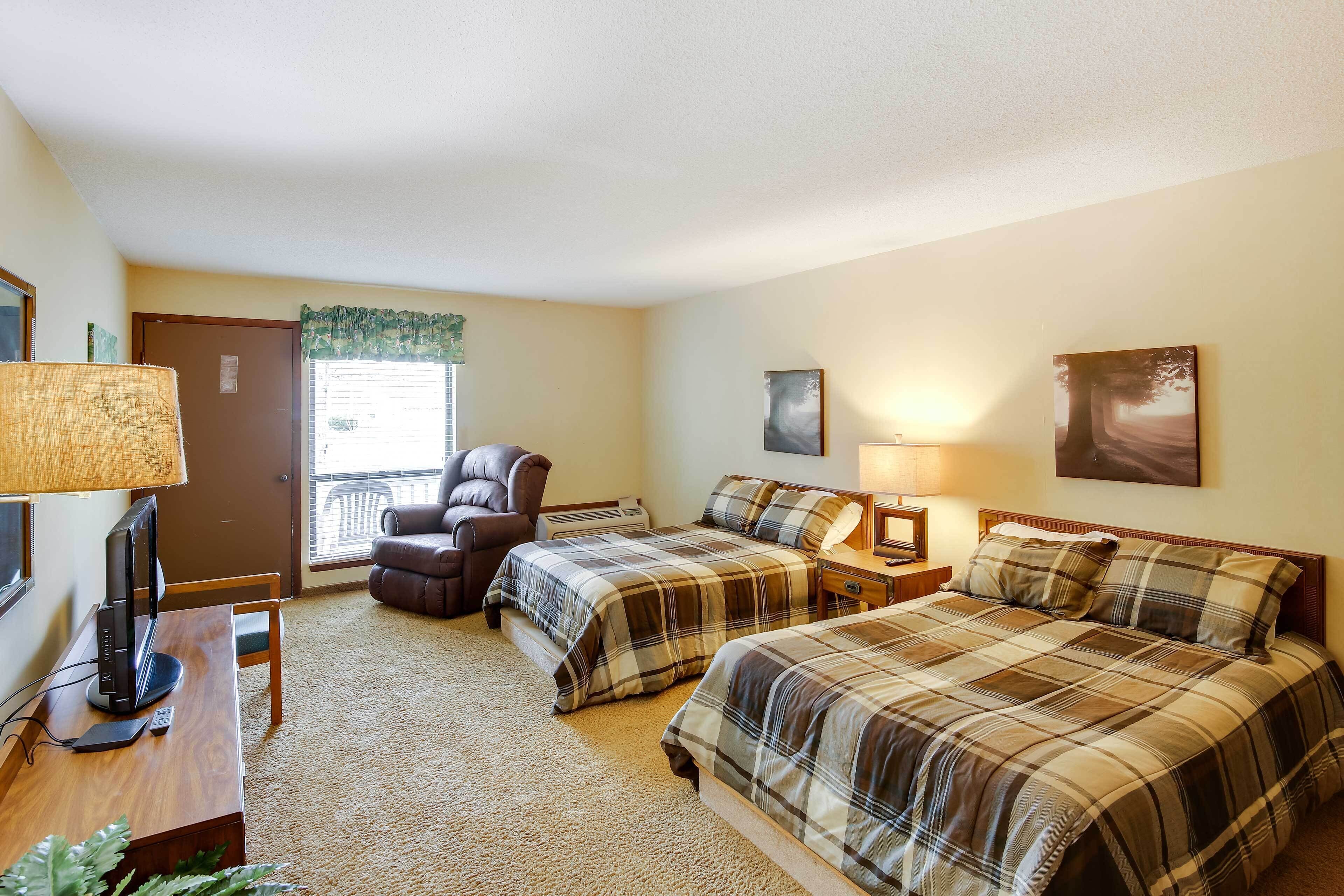 A hotel room with two beds, a desk with a computer, a chair, a TV, and a window with blinds.