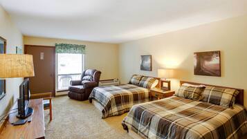 A hotel room with two beds, a desk with a computer, a chair, a TV, and a window with blinds.