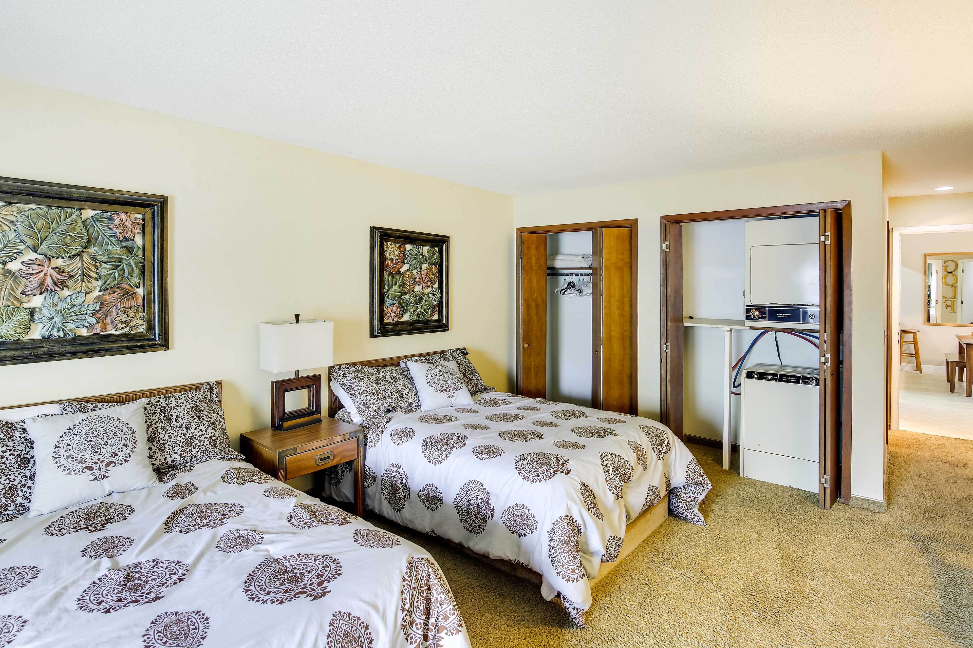 A hotel room with two beds, a nightstand, a dresser, a mirror, and a laundry area.