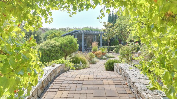 Un sentier de jardin qui mène à une pergola, d’où l’on peut admirer un bâtiment en arrière-plan.