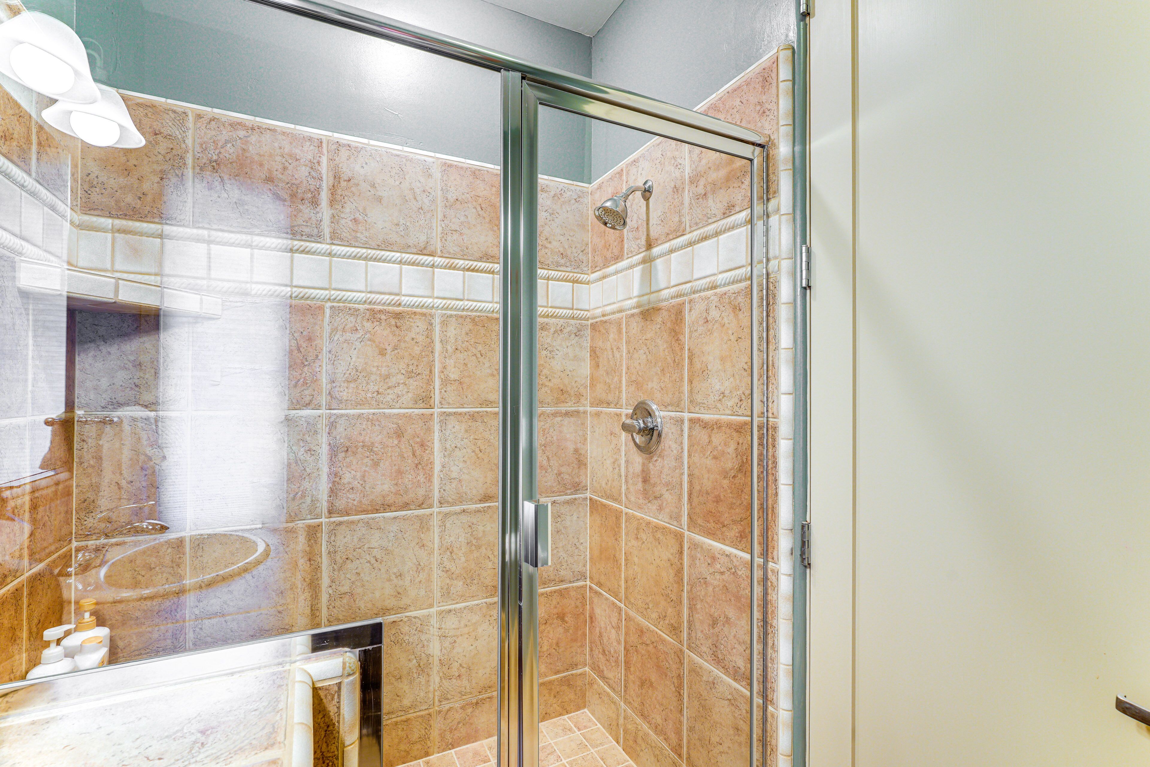 A modern bathroom with a glass shower enclosure, a marble-tiled wall, and a visible sink area.