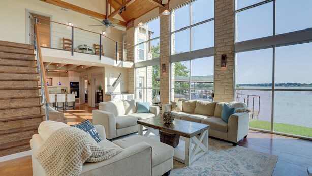 A spacious living area with a large window overlooking a body of water, a staircase leading to an upper level, and a cozy seating arrangement. - Waterfront Granbury House w/ Deck & Private Dock! (Granbury)