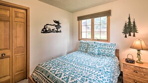 A bedroom with a bed, a wooden door, a window, and a wall decoration. - 'rocky Mountain Breezes' Cabin: Grill + Deck! (Estes Park)